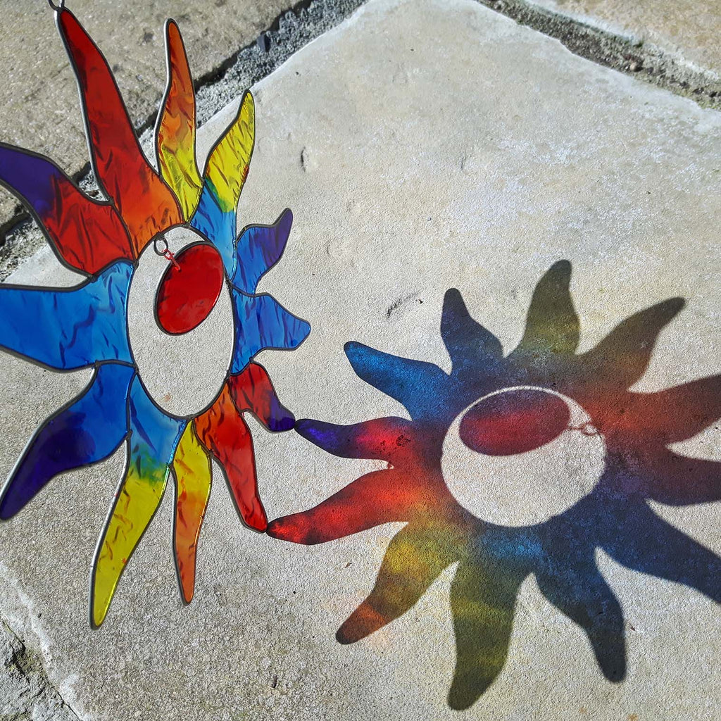 Sun-shaped suncatcher with twelve tapered rays in red, blue, yellow, green, orange and purple resin around a white centre, in a soldered metal frame
