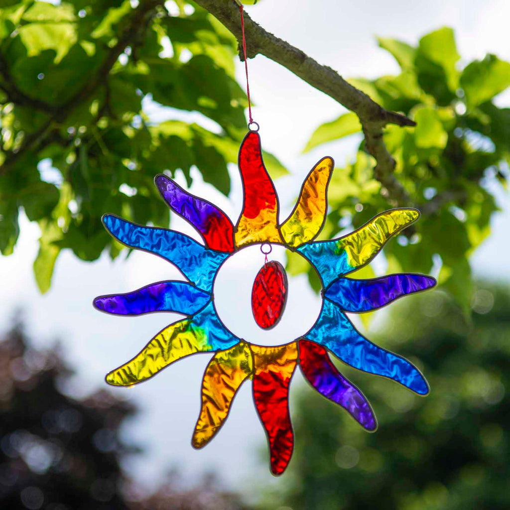 Sun-shaped suncatcher with twelve tapered rays in red, blue, yellow, green, orange and purple resin around a white centre, in a soldered metal frame
