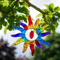 Sun-shaped suncatcher with twelve tapered rays in red, blue, yellow, green, orange and purple resin around a white centre, in a soldered metal frame