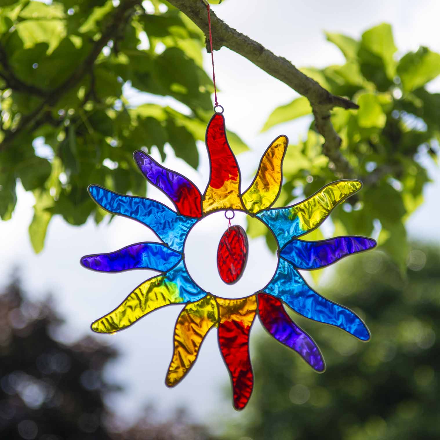 Sun-shaped suncatcher with twelve tapered rays in red, blue, yellow, green, orange and purple resin around a white centre, in a soldered metal frame