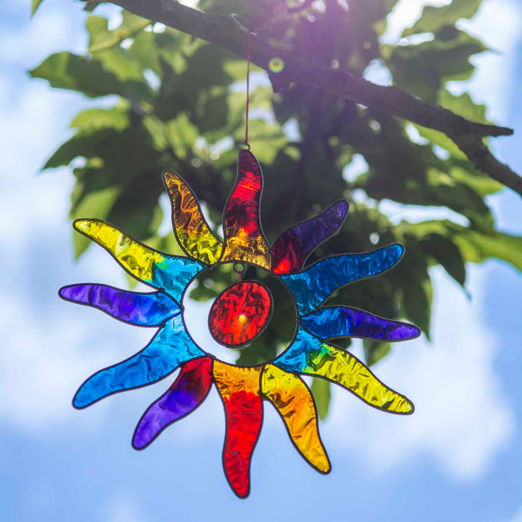 Sun-shaped suncatcher with twelve tapered rays in red, blue, yellow, green, orange and purple resin around a white centre, in a soldered metal frame