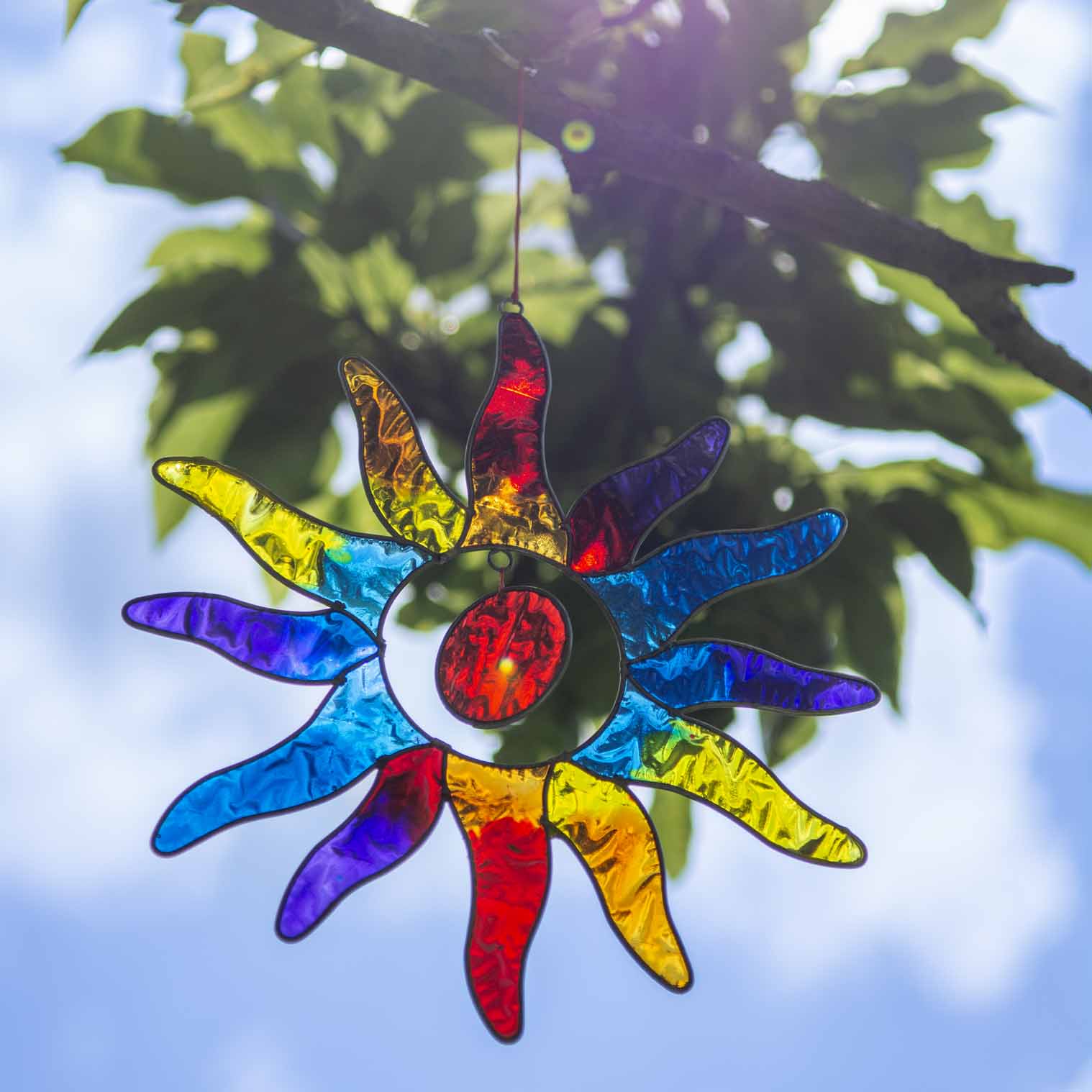Sun-shaped suncatcher with twelve tapered rays in red, blue, yellow, green, orange and purple resin around a white centre, in a soldered metal frame