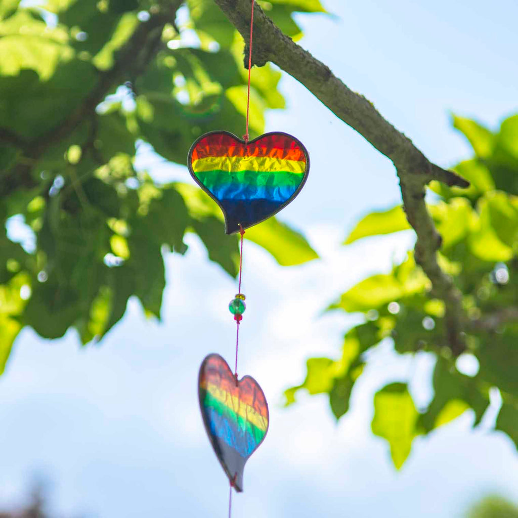 Vertical string of six rainbow-striped heart suncatchers in stained-glass effect resin, each with a small arrow detail at the top