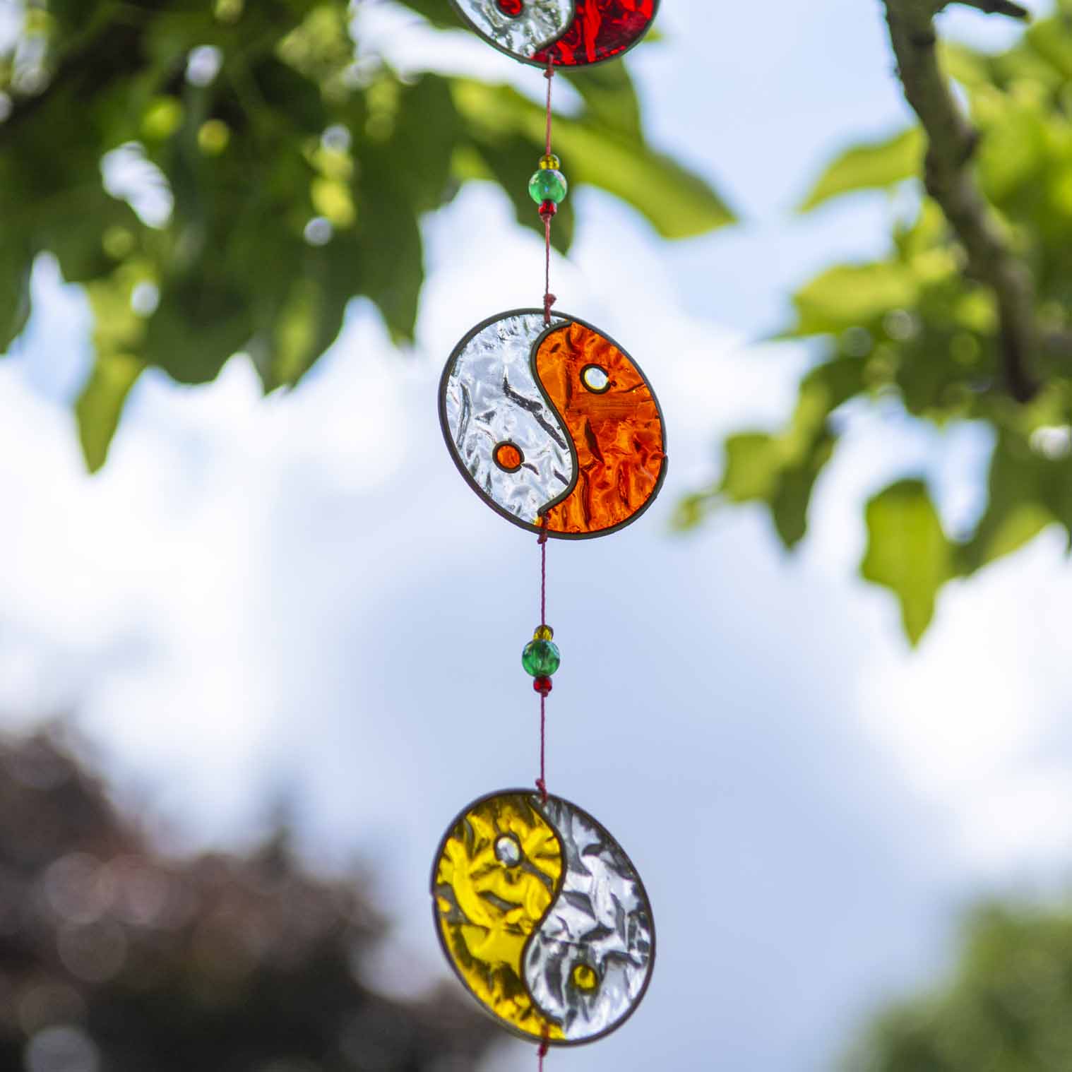 Vertical string of five yin yang suncatchers in contrasting colour pairings, with coloured beads strung between the discs