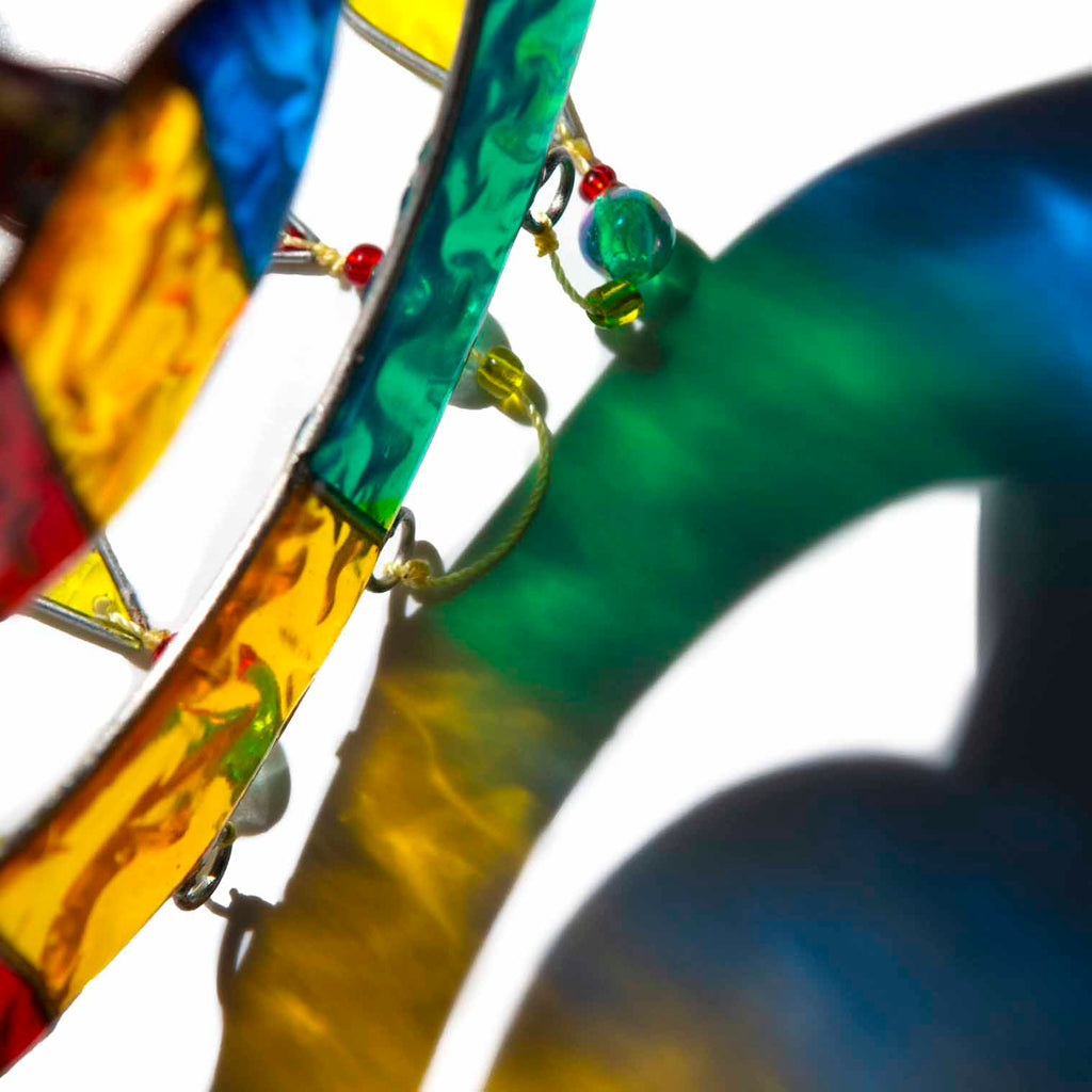 Suncatcher of two cheerful fish, a big one with a smaller fish inside, in bright primary colours with red, yellow and amber glass teardrops dangling beneath