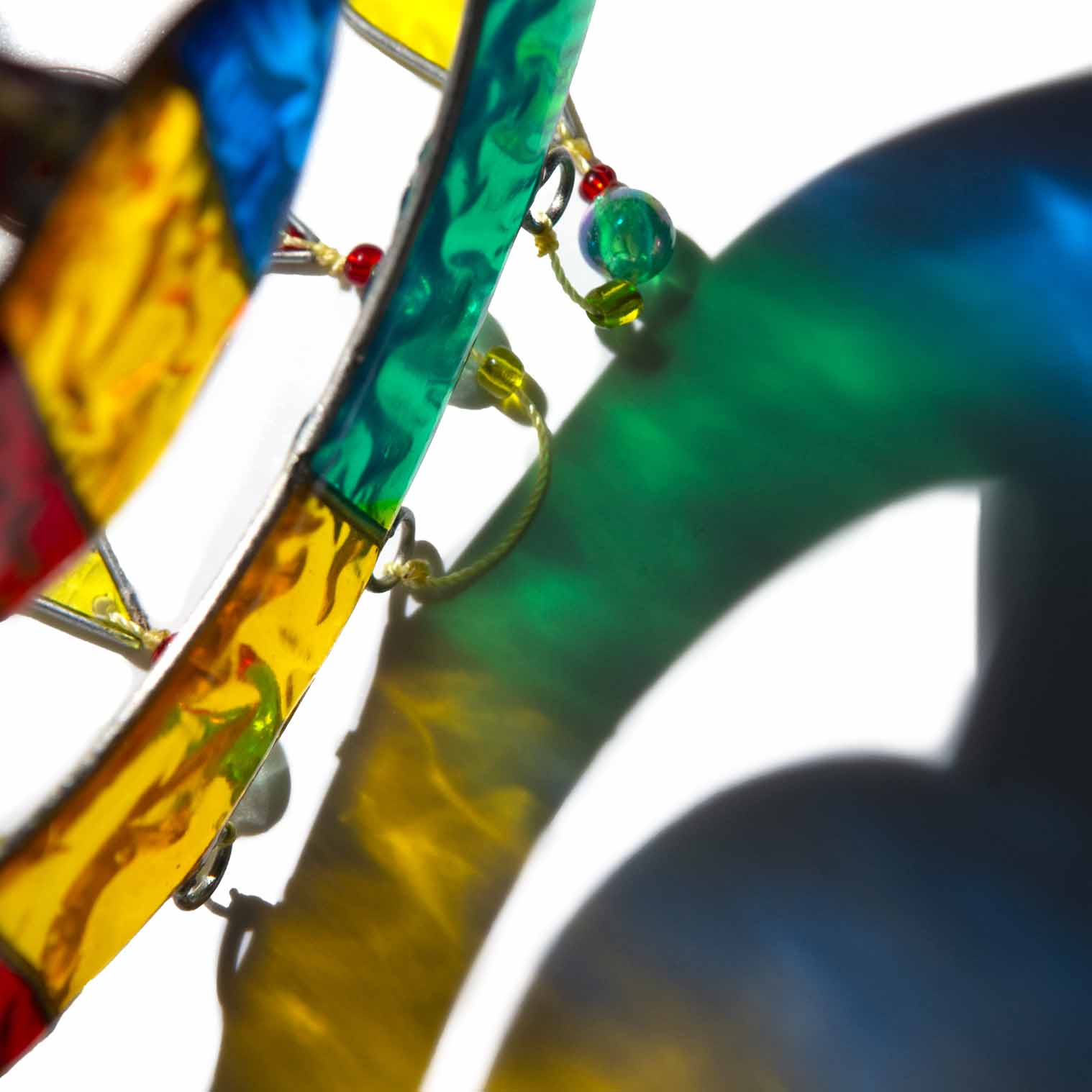 Suncatcher of two cheerful fish, a big one with a smaller fish inside, in bright primary colours with red, yellow and amber glass teardrops dangling beneath
