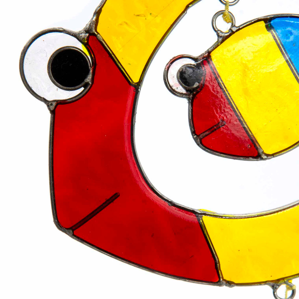 Suncatcher of two cheerful fish, a big one with a smaller fish inside, in bright primary colours with red, yellow and amber glass teardrops dangling beneath