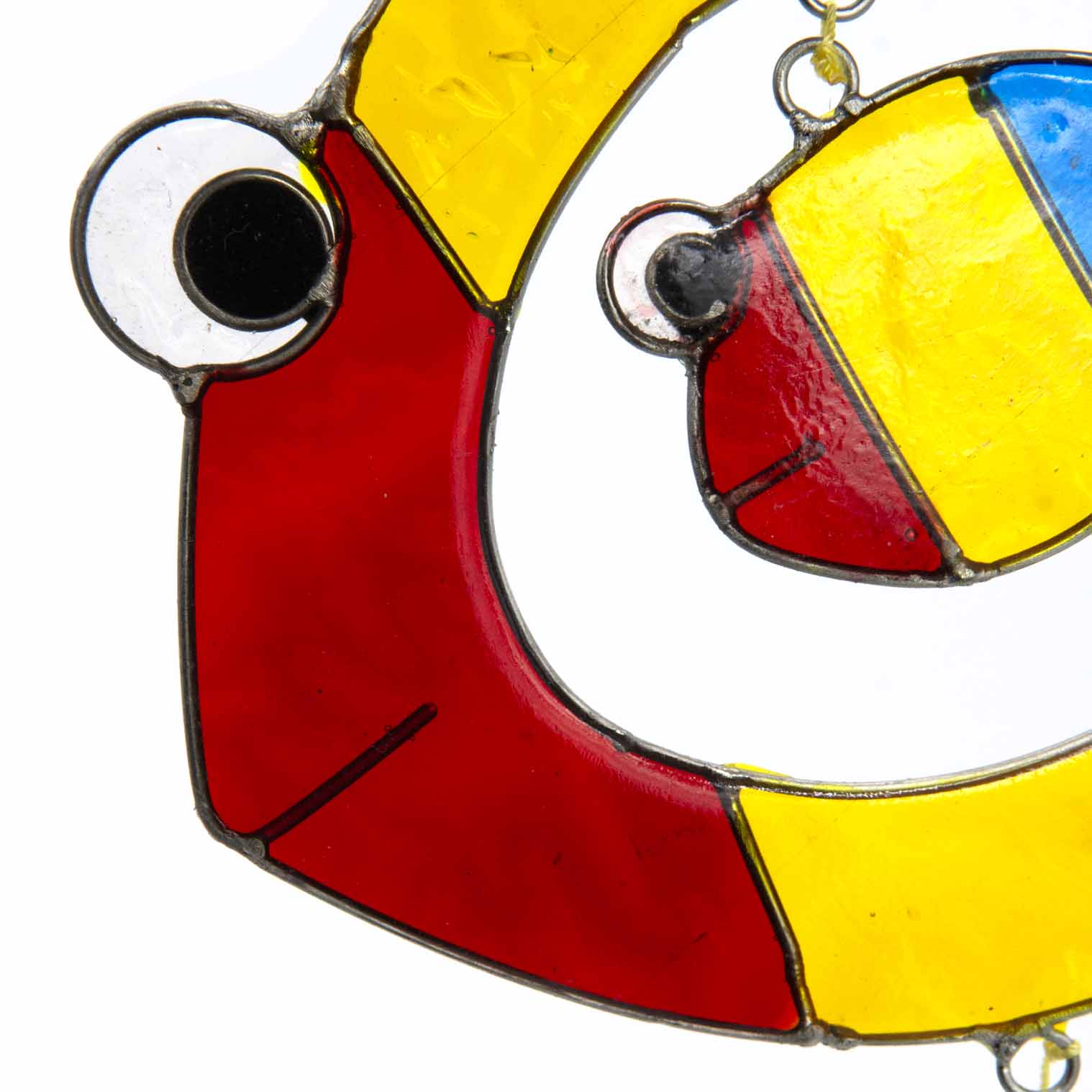 Suncatcher of two cheerful fish, a big one with a smaller fish inside, in bright primary colours with red, yellow and amber glass teardrops dangling beneath
