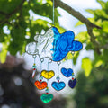 Blue resin cloud suncatcher with six threads of rainbow hearts dangling beneath in jewel tones of red, orange, yellow, green, blue and purple