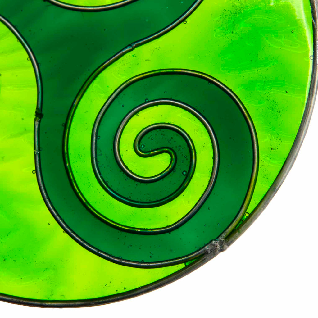 Round deep-green suncatcher with a Celtic triskele of three interlocking spirals, in a soldered metal frame