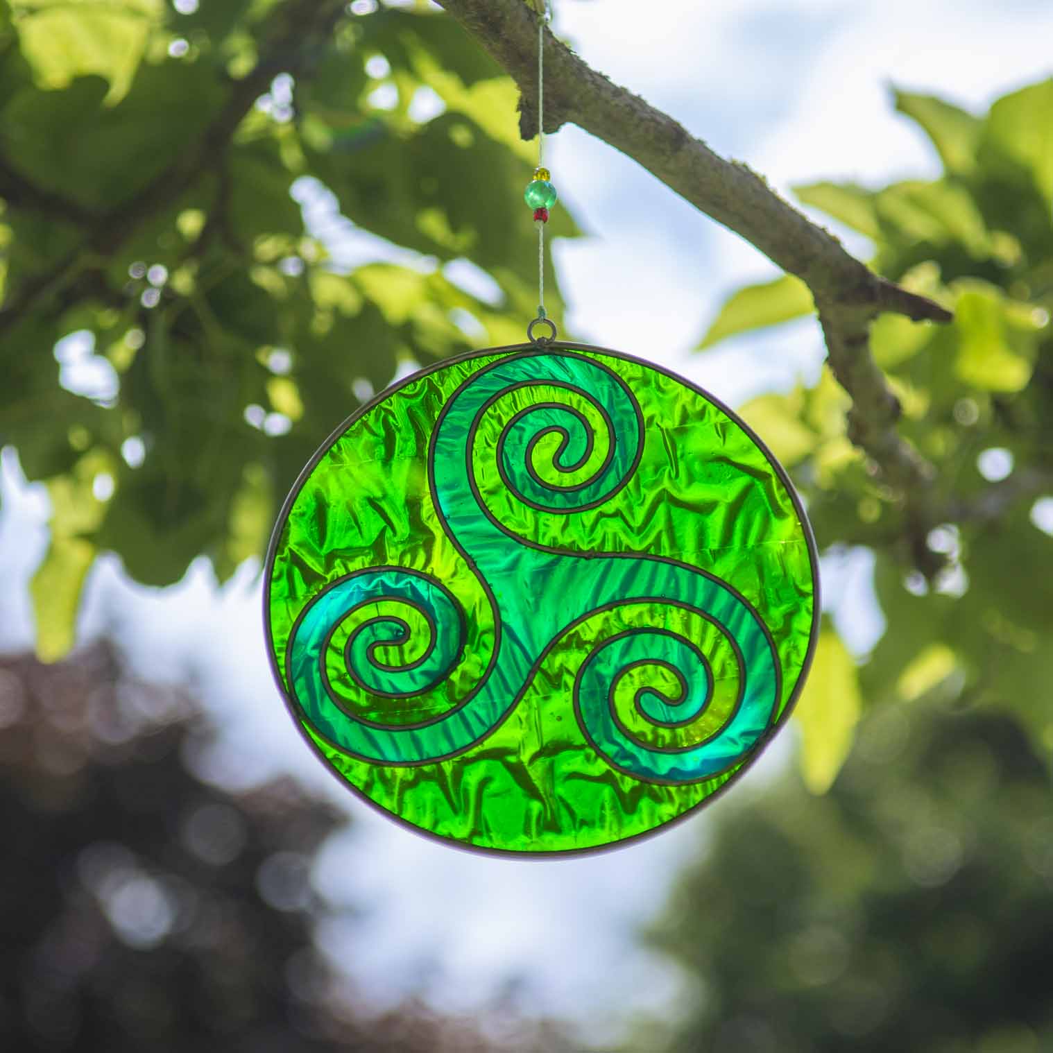 Round deep-green suncatcher with a Celtic triskele of three interlocking spirals, in a soldered metal frame
