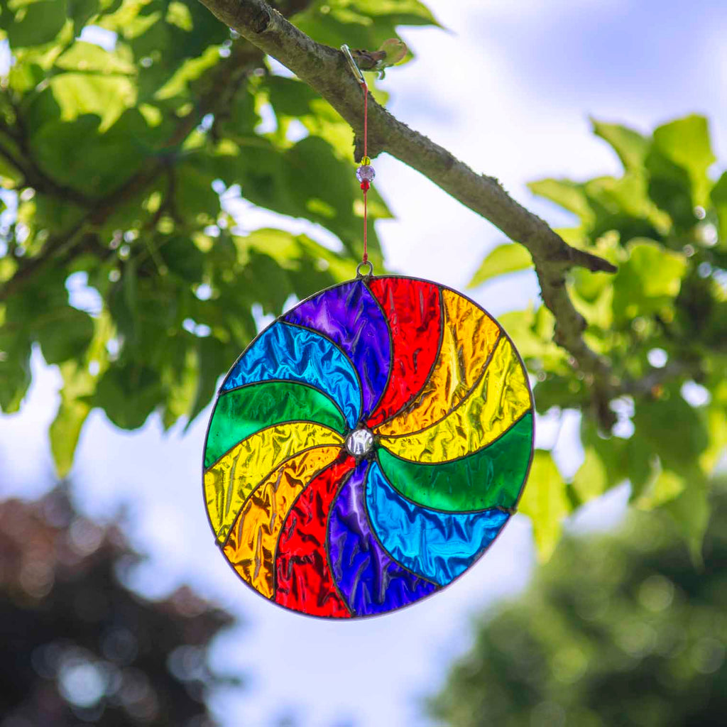 Round suncatcher with bold rainbow segments curving from the centre in a spinning pinwheel pattern, in a soldered metal frame