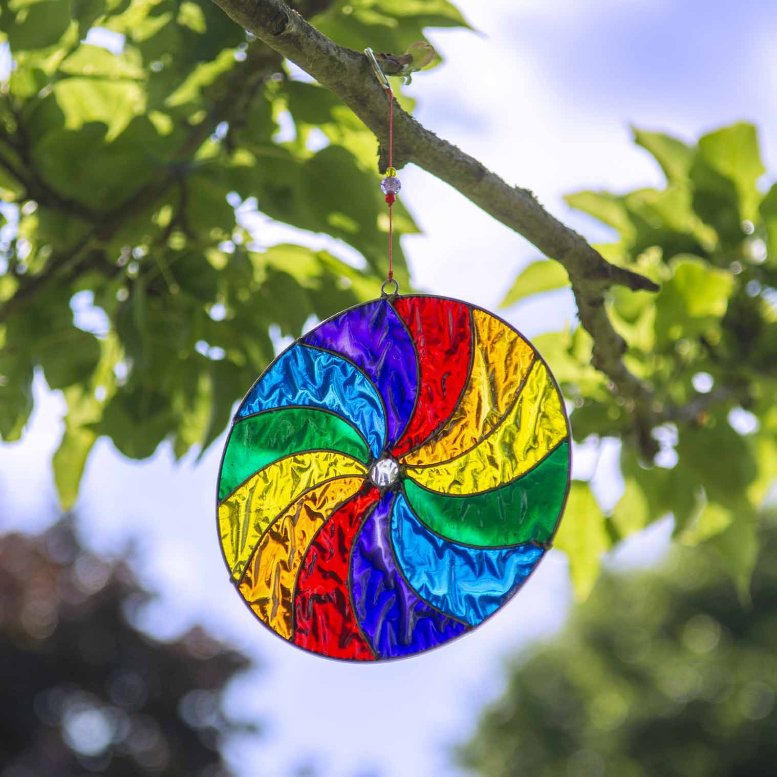 Round suncatcher with bold rainbow segments curving from the centre in a spinning pinwheel pattern, in a soldered metal frame