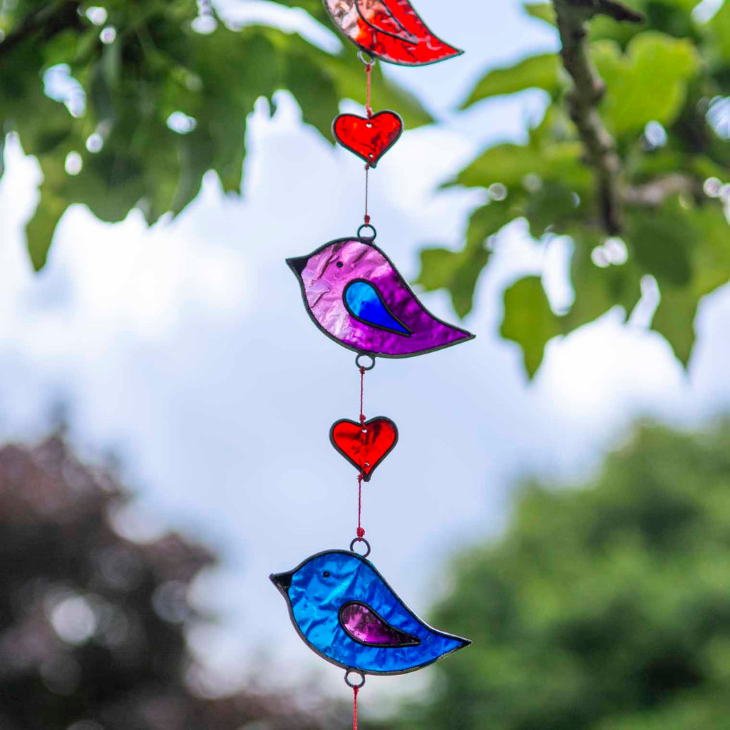 Vertical string of five jewel-tone bird suncatchers in red, pink, green, purple and blue, with small red hearts strung between them
