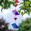 Vertical string of five jewel-tone bird suncatchers in red, pink, green, purple and blue, with small red hearts strung between them