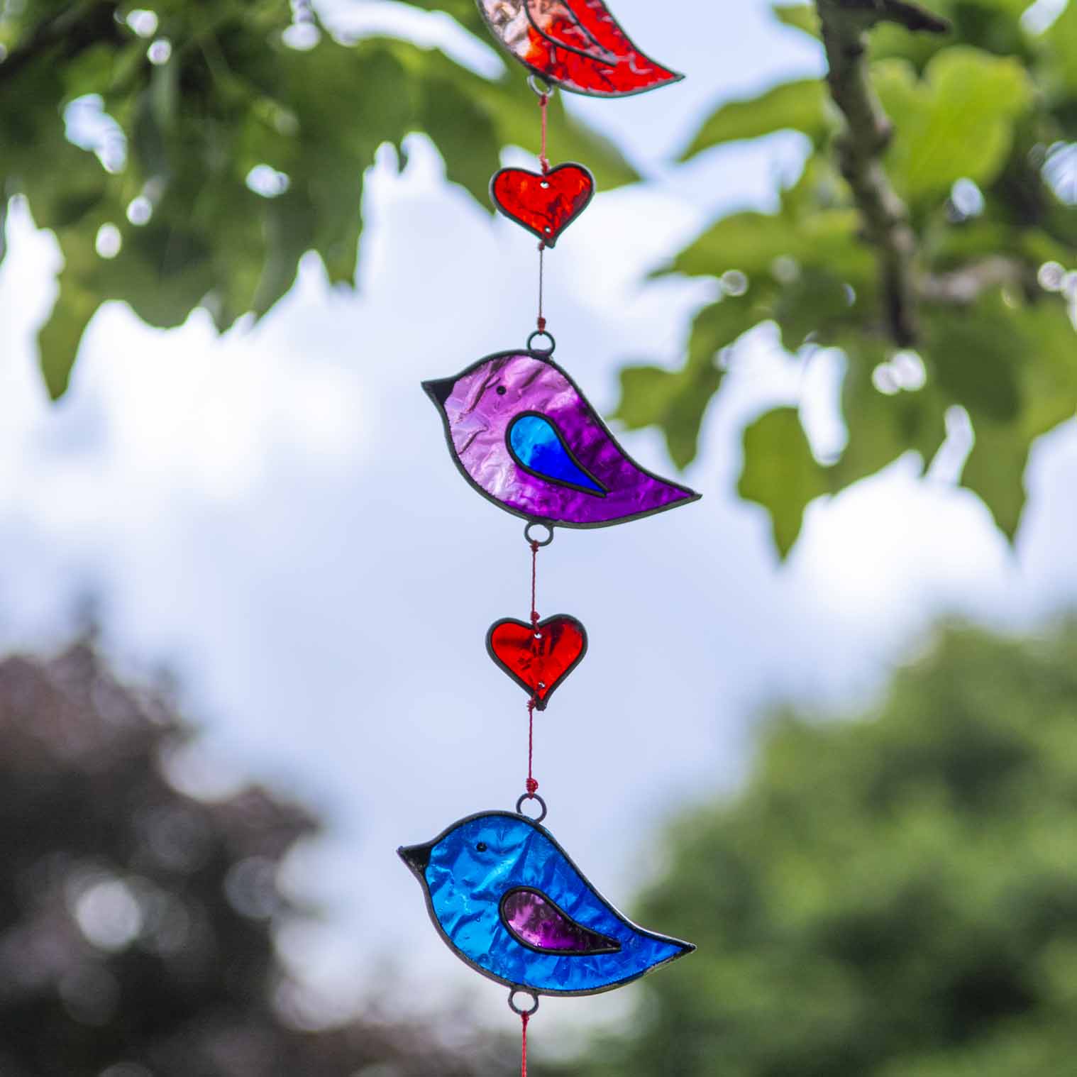 Vertical string of five jewel-tone bird suncatchers in red, pink, green, purple and blue, with small red hearts strung between them
