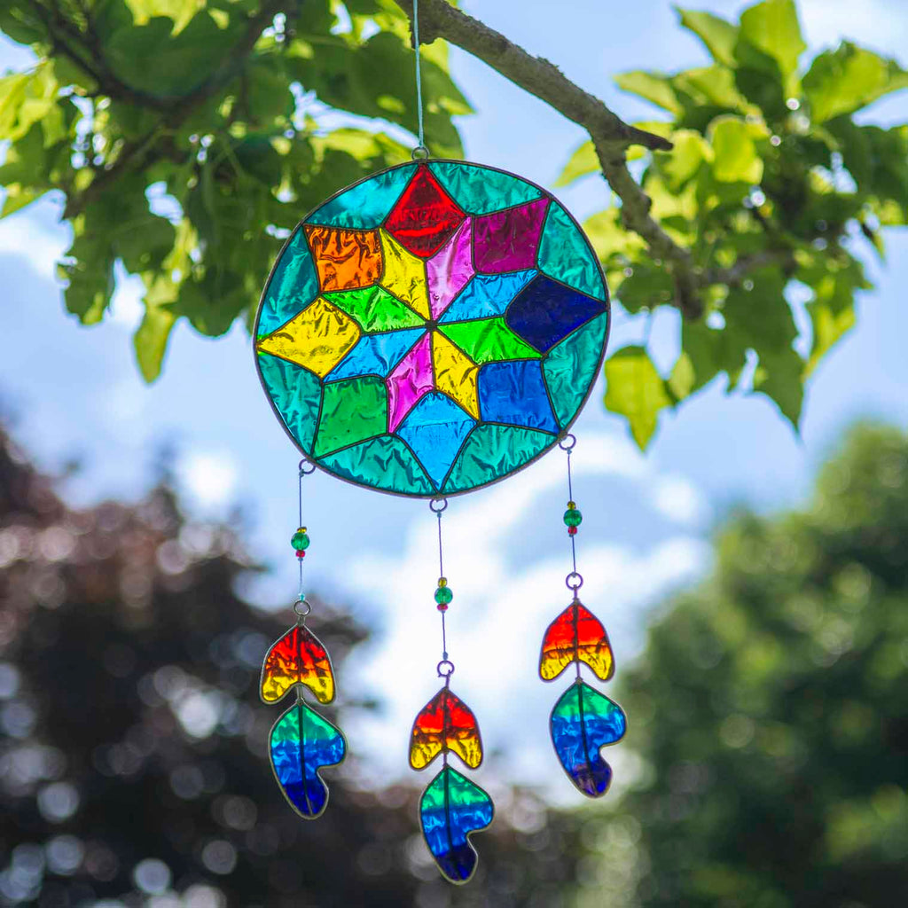 Round dreamcatcher-style suncatcher with a geometric resin web in blue, green, ruby and amber, with three rainbow feather pieces dangling beneath