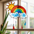 Stained-glass effect suncatcher of a red sun rising over a rainbow arc, with two clouds and dangling red, yellow and blue raindrop pendants