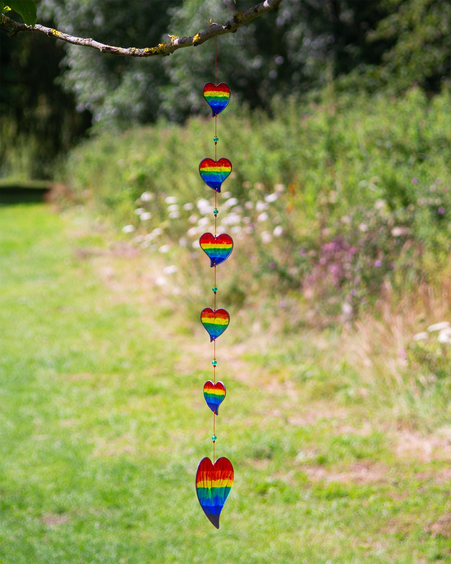 Vertical string of six rainbow-striped heart suncatchers in stained-glass effect resin, each with a small arrow detail at the top