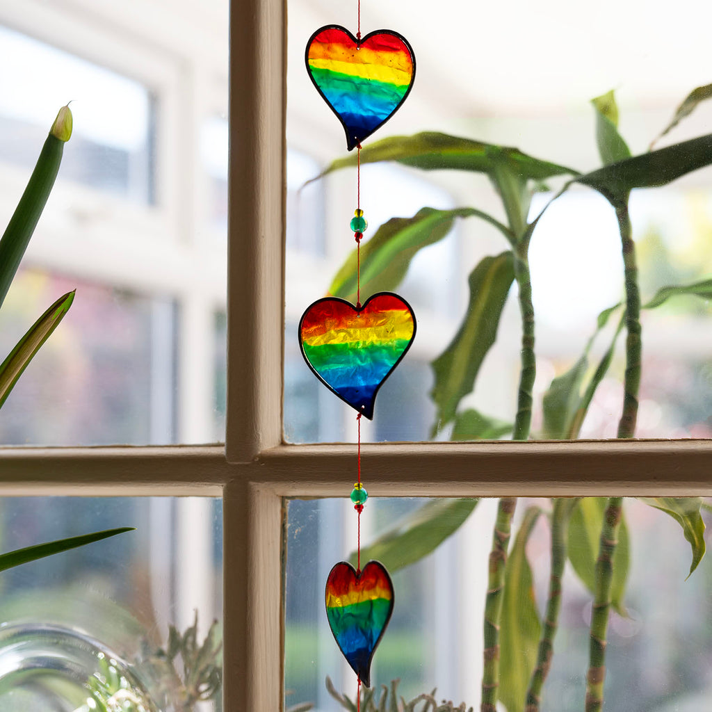 Vertical string of six rainbow-striped heart suncatchers in stained-glass effect resin, each with a small arrow detail at the top