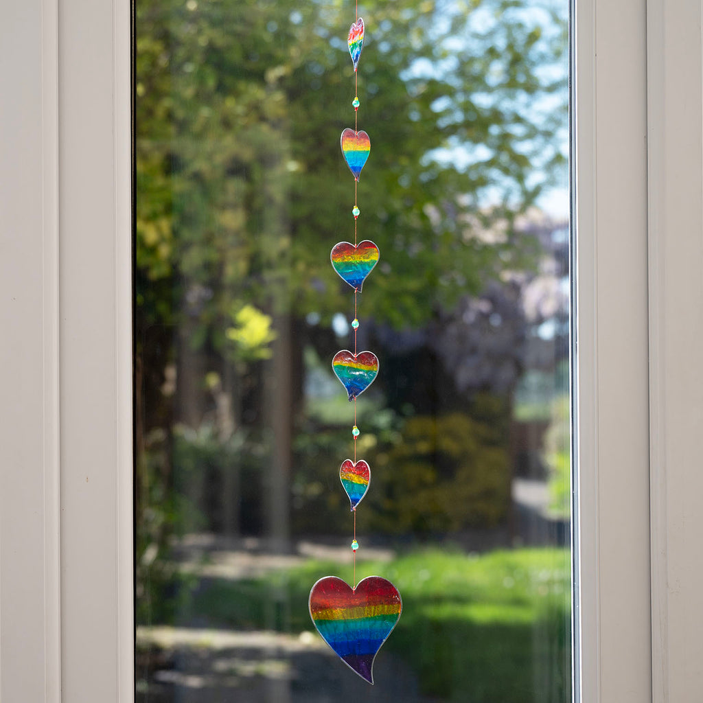 Vertical string of six rainbow-striped heart suncatchers in stained-glass effect resin, each with a small arrow detail at the top