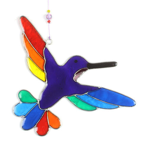 Hummingbird suncatcher in mid-flight with a blue and turquoise body and a fan of rainbow tail feathers, in a hand-shaped soldered metal frame