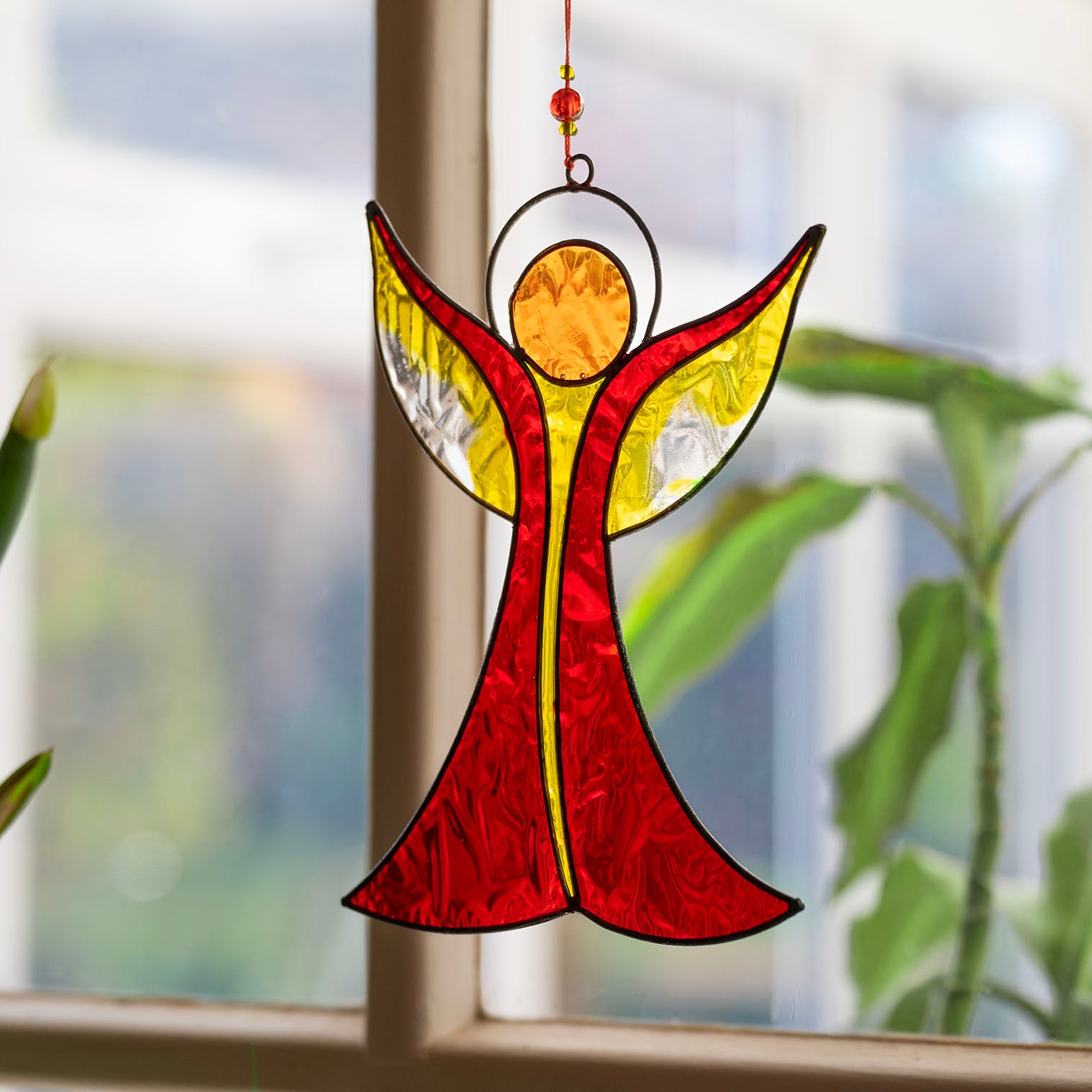 Angel-shaped suncatcher in warm red and amber resin with outstretched wings rising to a halo, in a soldered metal frame