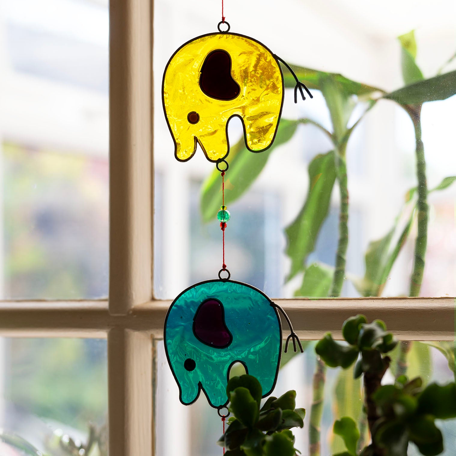 Vertical string of five jewel-tone elephant suncatchers in red, yellow, green, blue and purple, in soldered metal frames