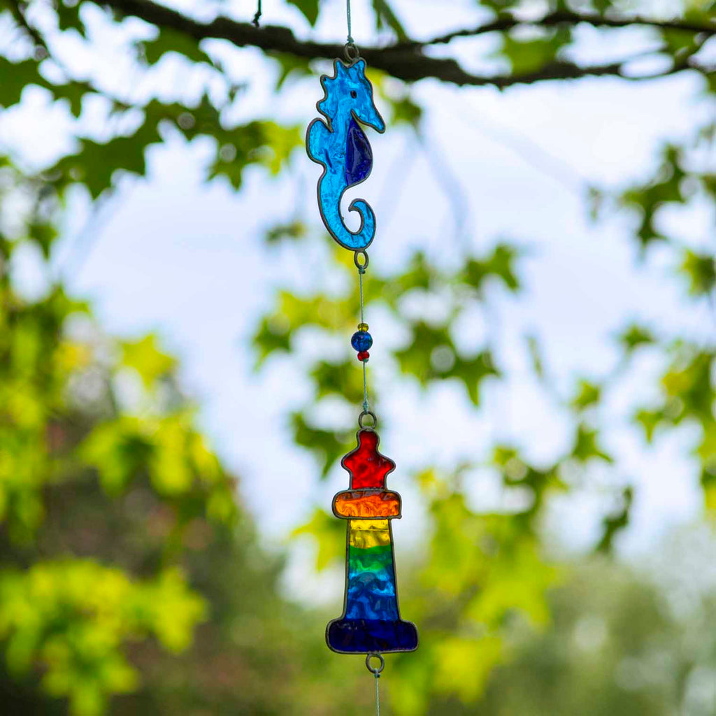 Nautical hanging suncatcher with a blue seahorse, a deep blue anchor and a red striped lighthouse strung vertically in soldered metal frames