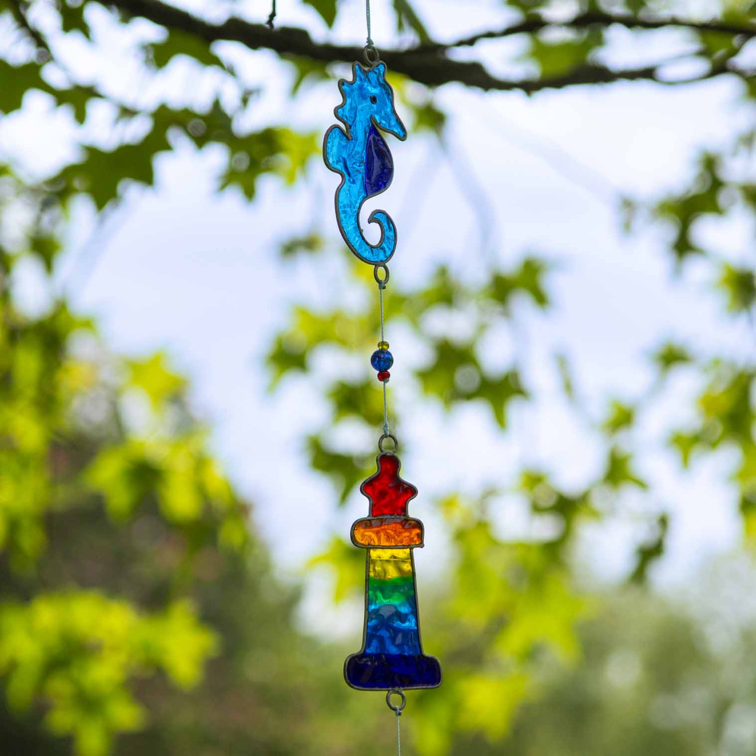 Nautical hanging suncatcher with a blue seahorse, a deep blue anchor and a red striped lighthouse strung vertically in soldered metal frames