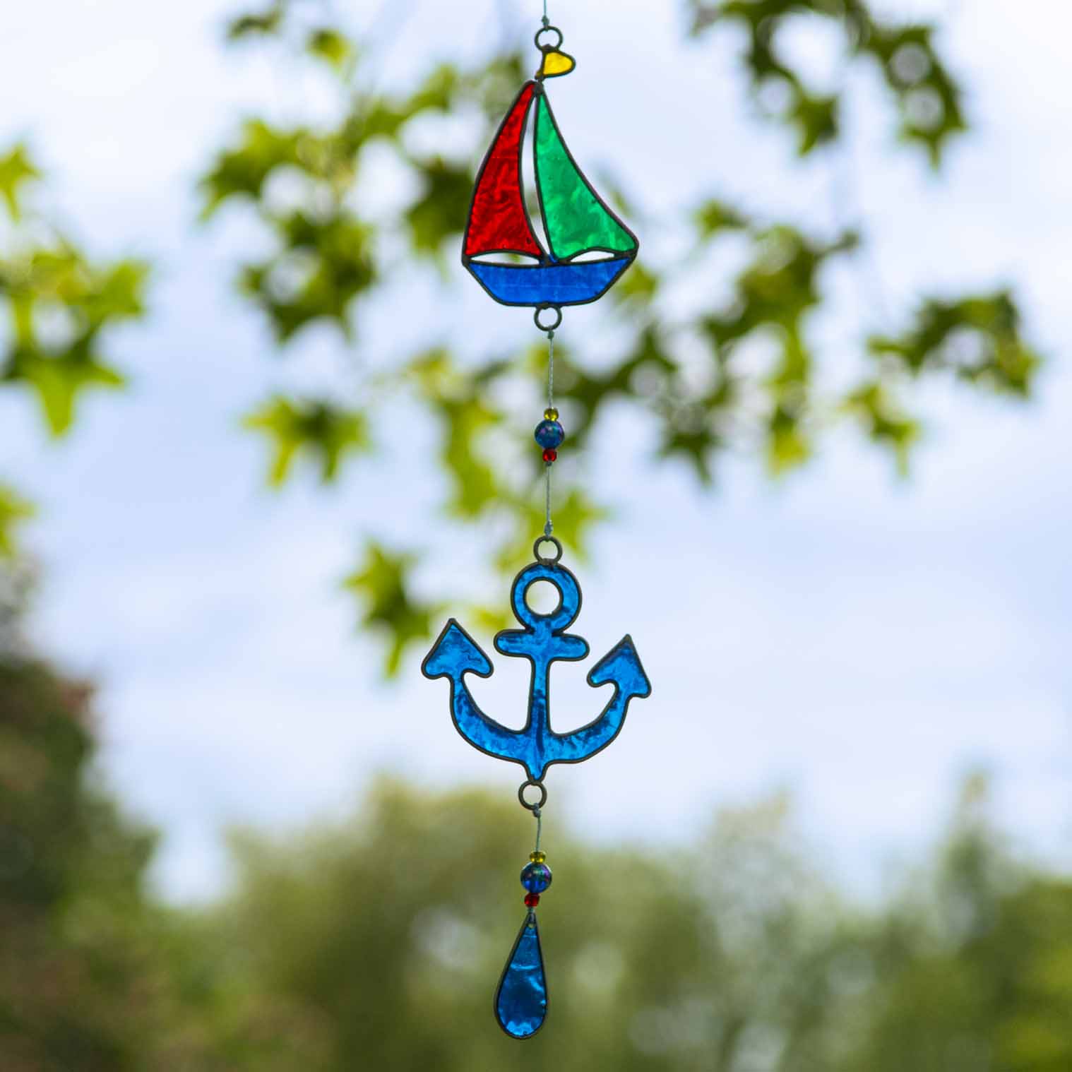 Nautical hanging suncatcher with a blue seahorse, a deep blue anchor and a red striped lighthouse strung vertically in soldered metal frames