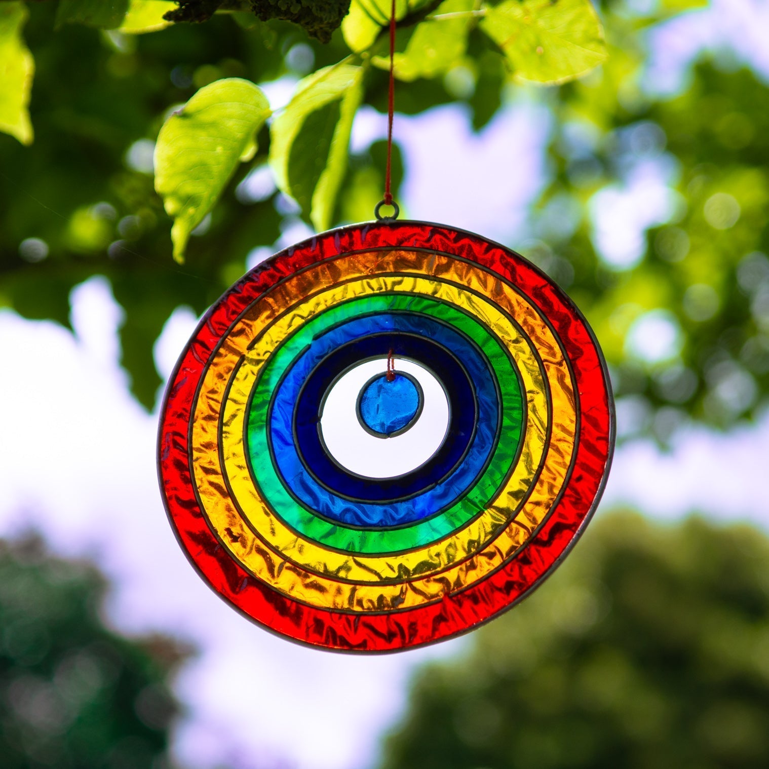 Round suncatcher with concentric rings of rainbow colour radiating from a deep blue centre, in a soldered metal frame