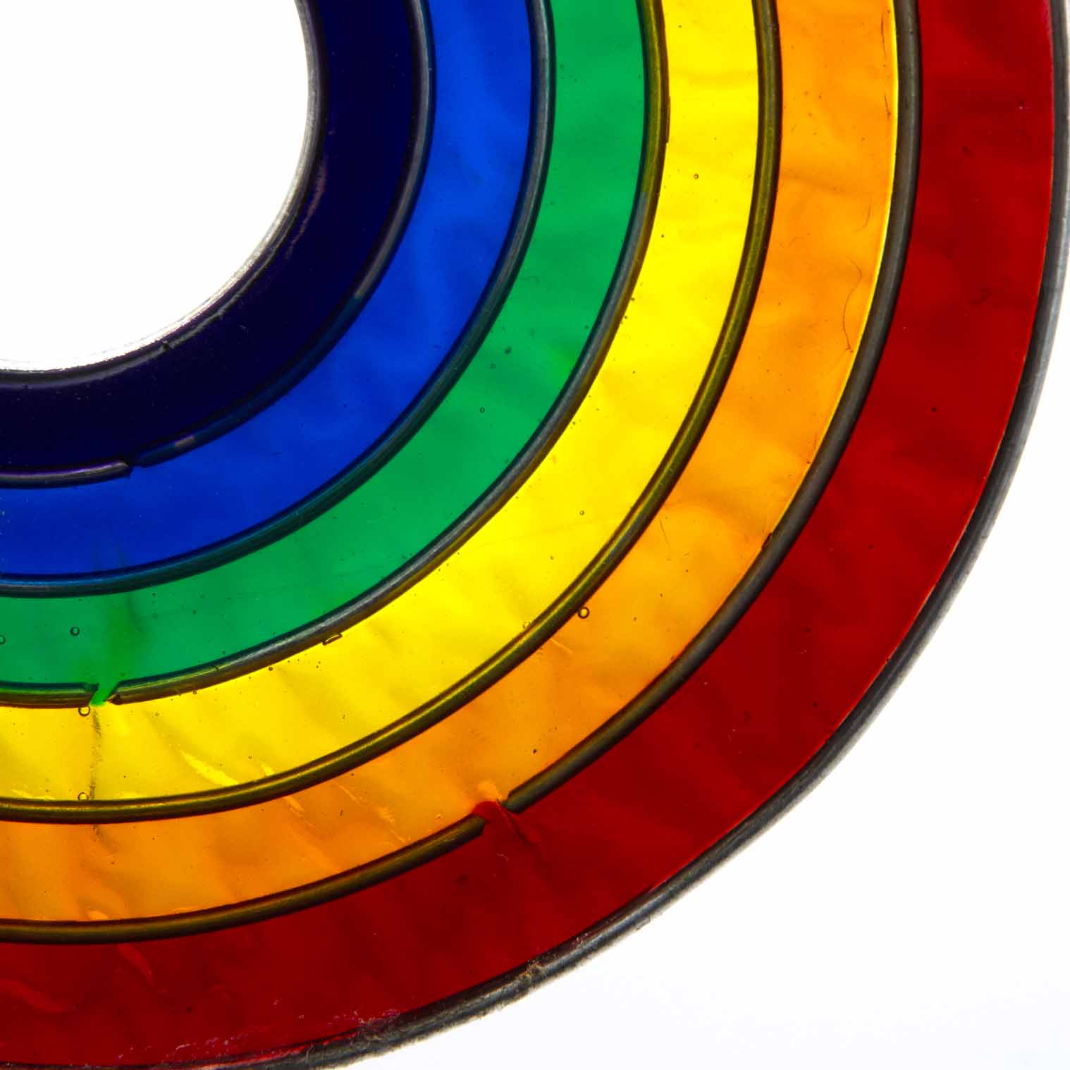 Round suncatcher with concentric rings of rainbow colour radiating from a deep blue centre, in a soldered metal frame