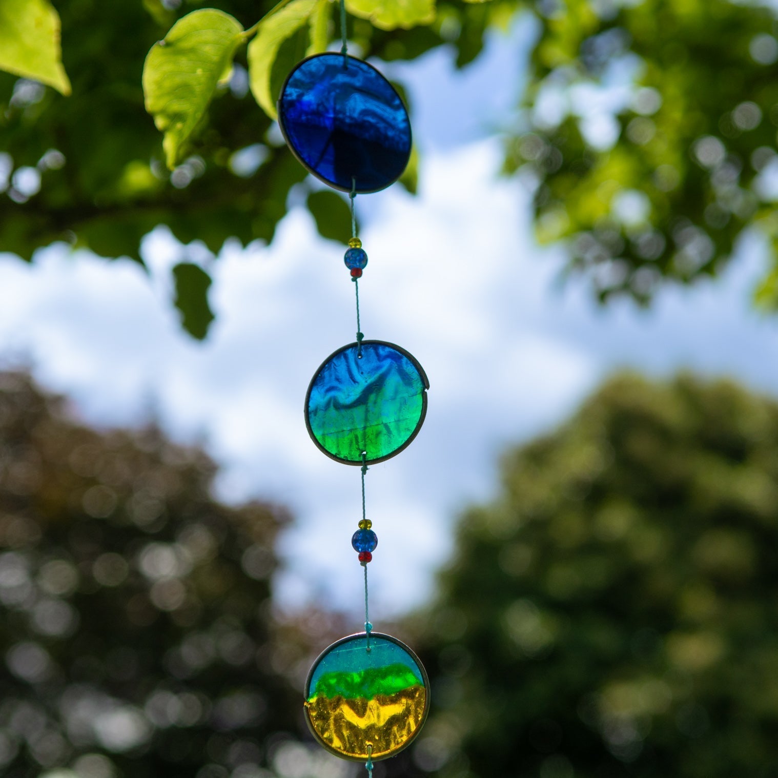 Vertical cascade of six resin discs swirled from deep blue through teal and green to warm orange, with bright glass beads between them